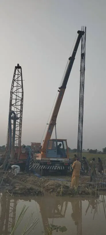 Rotary piling rig and crane lowering a pile cage beside waterlogged ground